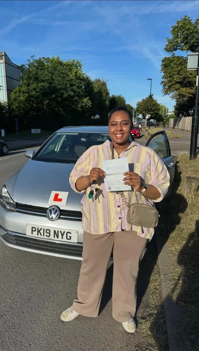 Smiling woman holding her pass certificate and car keys beside a silver Volkswagen Golf with L-plates